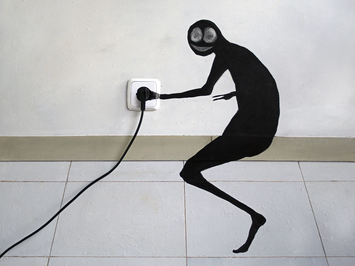 Figura negra pintada en la pared enchufando un cable a una toma de corriente